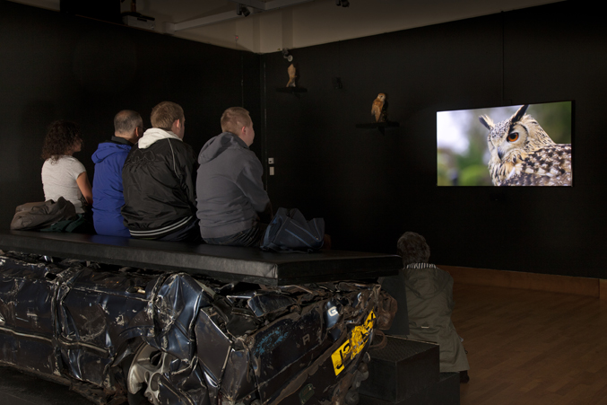 Photo of people watching a video at Jeremy Deller's English Magic exhibition at Bristol Museum & Art Gallery
