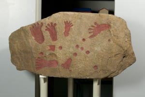 Image of a slab of rock with red footprints and handprints on it