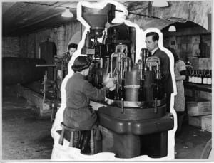Black and white photograph of a seated woman and standing man working a machine in a basement