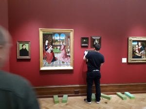 A technician in the process of hanging a painting next to the Bouts 