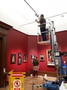  A man stood on a cherry picker working on the lighting in the gallery.
