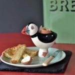 Egg cup in the shape of a Puffin bird. The egg cup is surrounded by toast and egg.