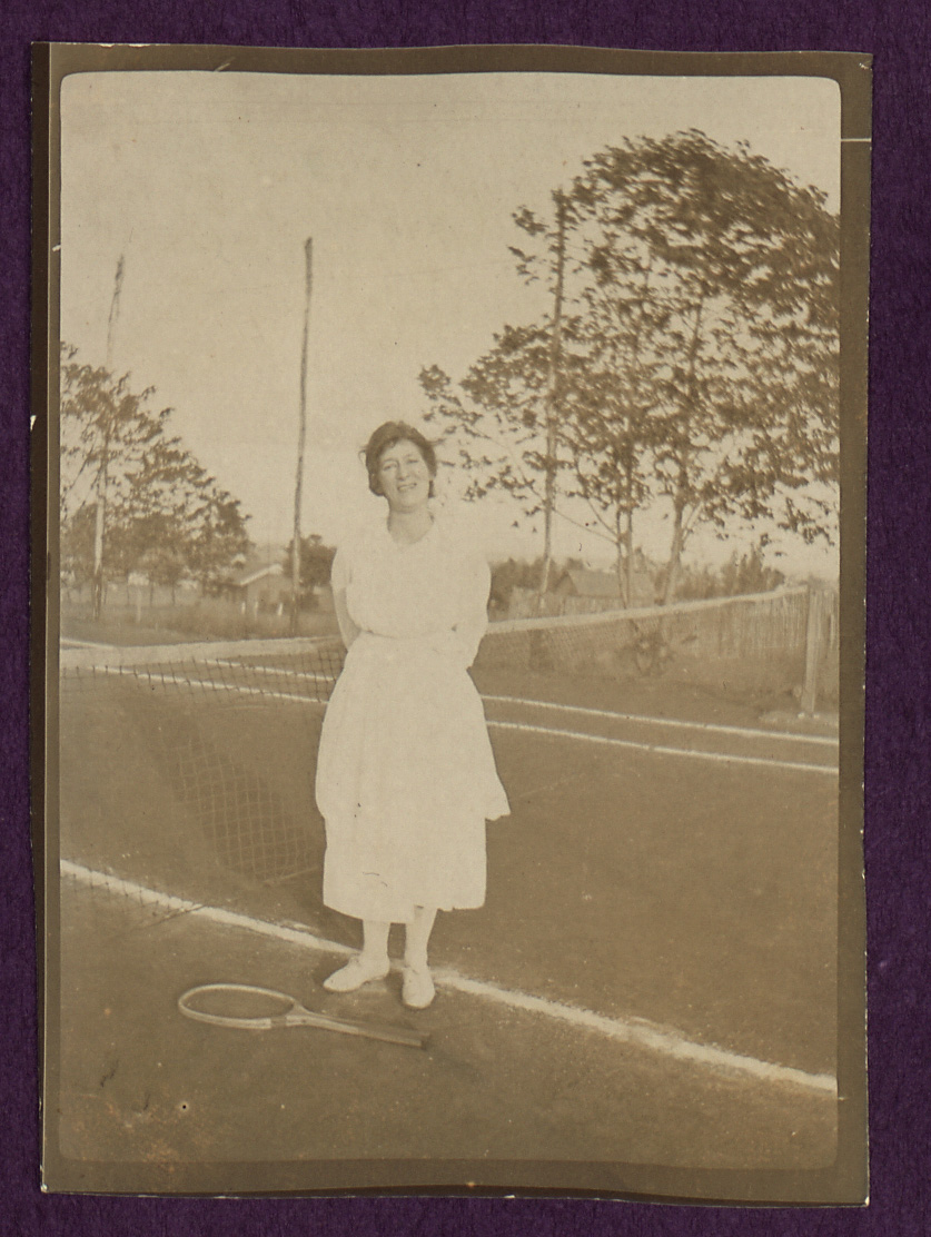 Old photograph of Maud Harpham, one of the women mentioned in the diary. She's stood on a tennis court with her racket lead on the ground. 