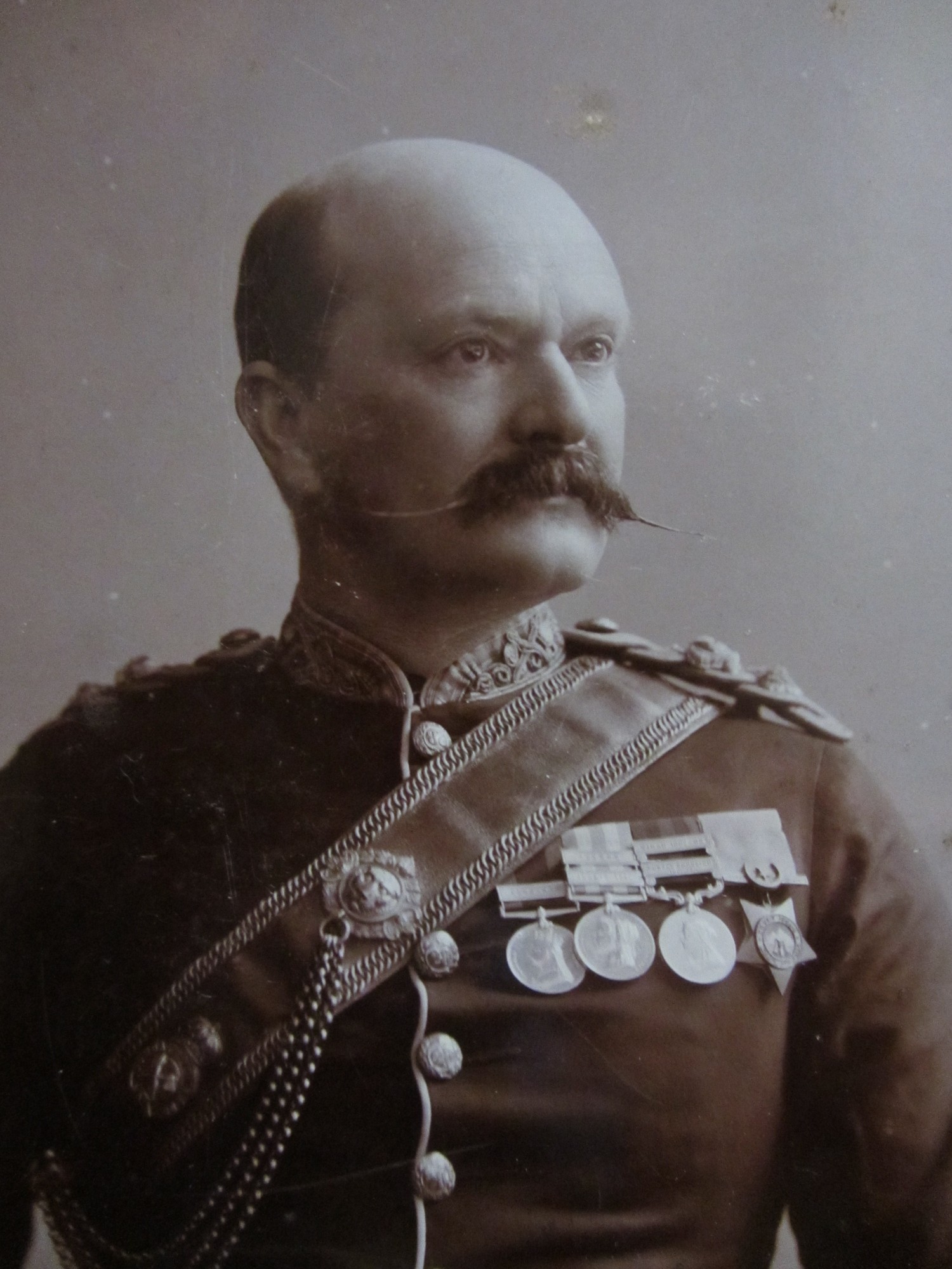 Old fashioned image of a bald man, with a large mustache and dressed in military uniform. 