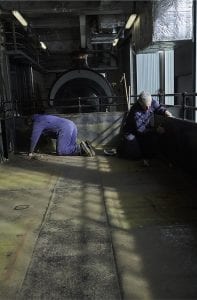 Two men in overalls on their hands and knees working on a steam train at M Shed