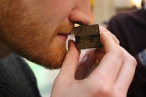 A man with a beard sniffing a miniature cube of tea designed to look like Ai Weiwei's Ton of Tea