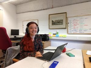 Smiling woman wearing headphones sat in front of a laptop