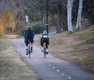 Two people cycling on a road with frosty looking grass on either side