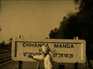 Photograph of a man in traditional clothes pointing to a railway sign