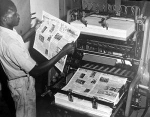 machine operator checks the inking on a page of newsprint