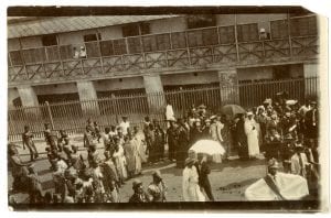 Photograph of a large crowd of people in Ghana taking part in a masquerade dressed in British costume