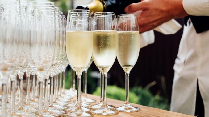 A table of champagne flutes being filled by a male waiter