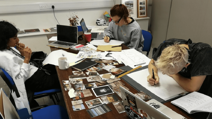Anika, Marcin and Maisie working around a large table covered in photographs and paperwork