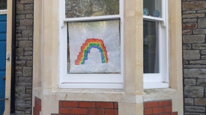 Photograph of the outside of a house with a child's painting of a rainbow on the window