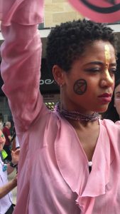 Photograph of person in extinction rebellion march with the XR symbol drawn on their cheek