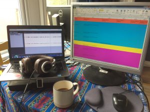 A computer screen, laptop, headphones and a cup of coffee on a desk