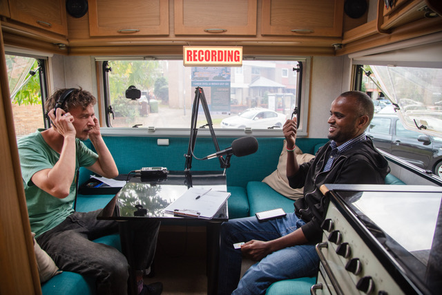 Two men sat opposite each other recording audio in a motorhome
