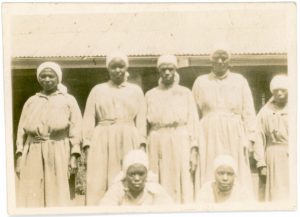 Black and white faded image. Seven nurses all dressed in long gowns.