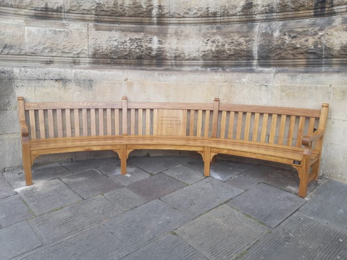 A curved oak war memorial bench sitting in an alcove outside Bristol Museum & Art Gallery