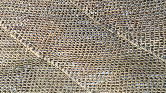 A close up of a bag made of looped and netted vegetable fibre with diagonal stripes woven into the body.