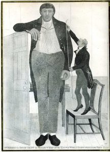 A print of O'Brien. All of the pictures we have of him look very different. This one shows him as a heaviliy- built man in the centre of the picture. He leans on an open door to his left and faces the viewer, smiling slightly. On his right, a much smaller man stands on a chair, measuring his height. O'Brien wears grey breeches, shoes, a finely-striped shirt and long black coat.