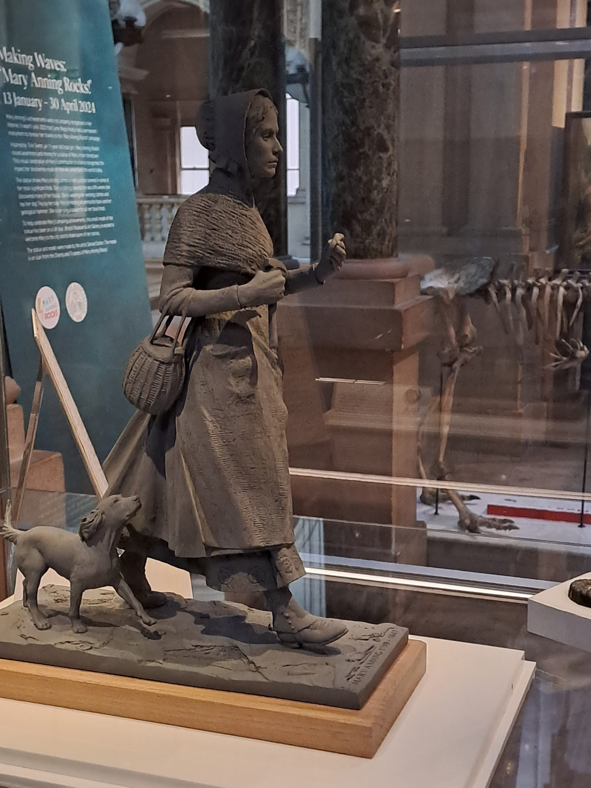small maquette of Mary Anning with a small dog beside here. In a glass cabinet