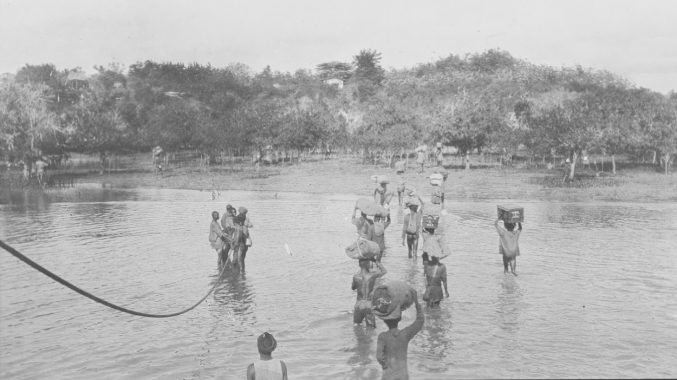 black and white photo of people wading through water unloading a ship