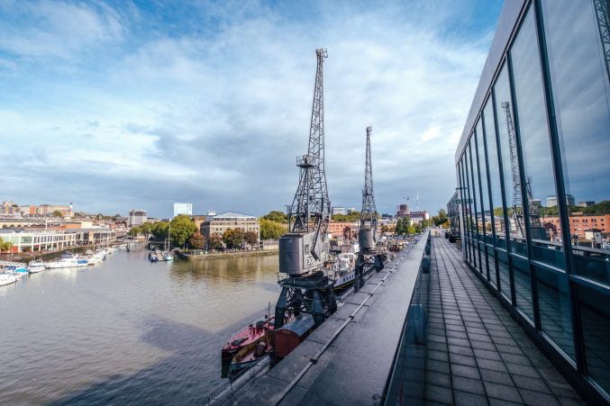 a view of the Bristol harborside, with two electric cranes in the foreground, from m shed's balcony