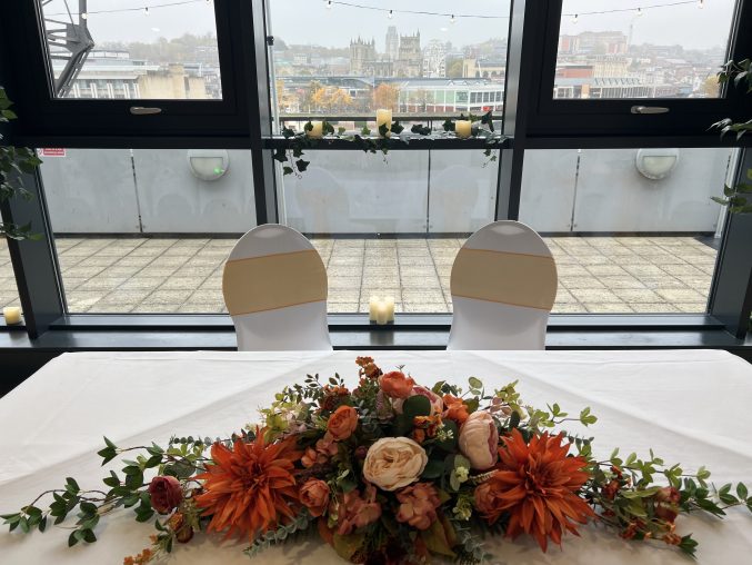 a table with flowers and two chairs set up for a wedding ceremony with a view of Bristol from a balcony behind