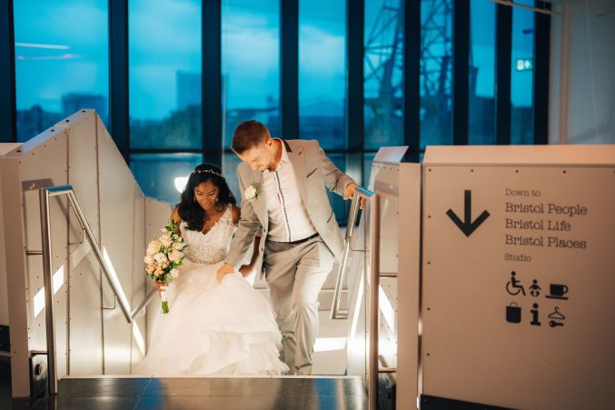 a bride and groom walk up the stairs at M Shed on their wedding day
