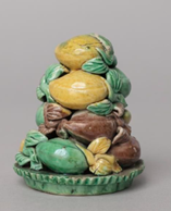 A plate holding a small tower of ceramic fruit in bright greens, yellows and browns. 