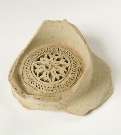 A shard of light coloured pottery, with an intricate design carved in a circle. 