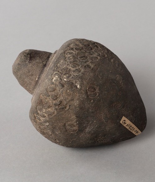 A dark brow matte piece of pottery in the shape of a grenade, with a scale-like pattern carved into the surface. 