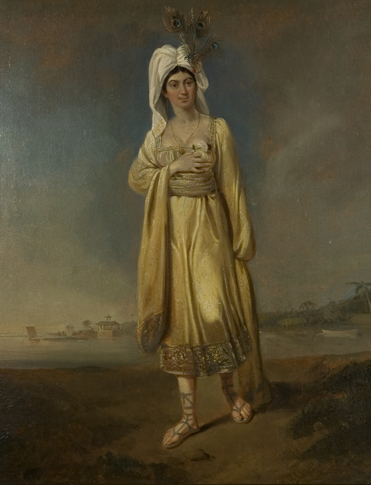 A woman standing on a beach wearing a dress and turban.