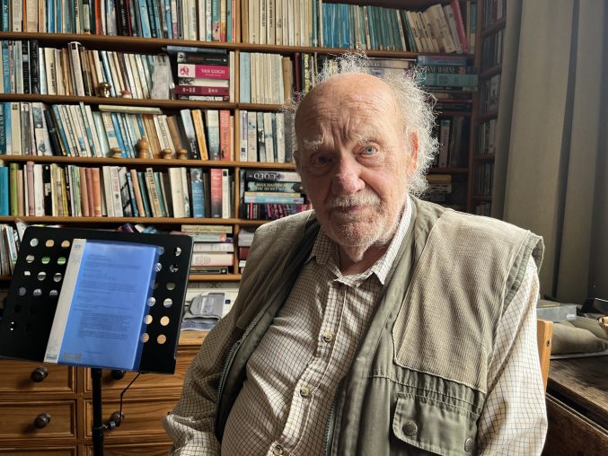 An old man man sitting in a library next to a music stand