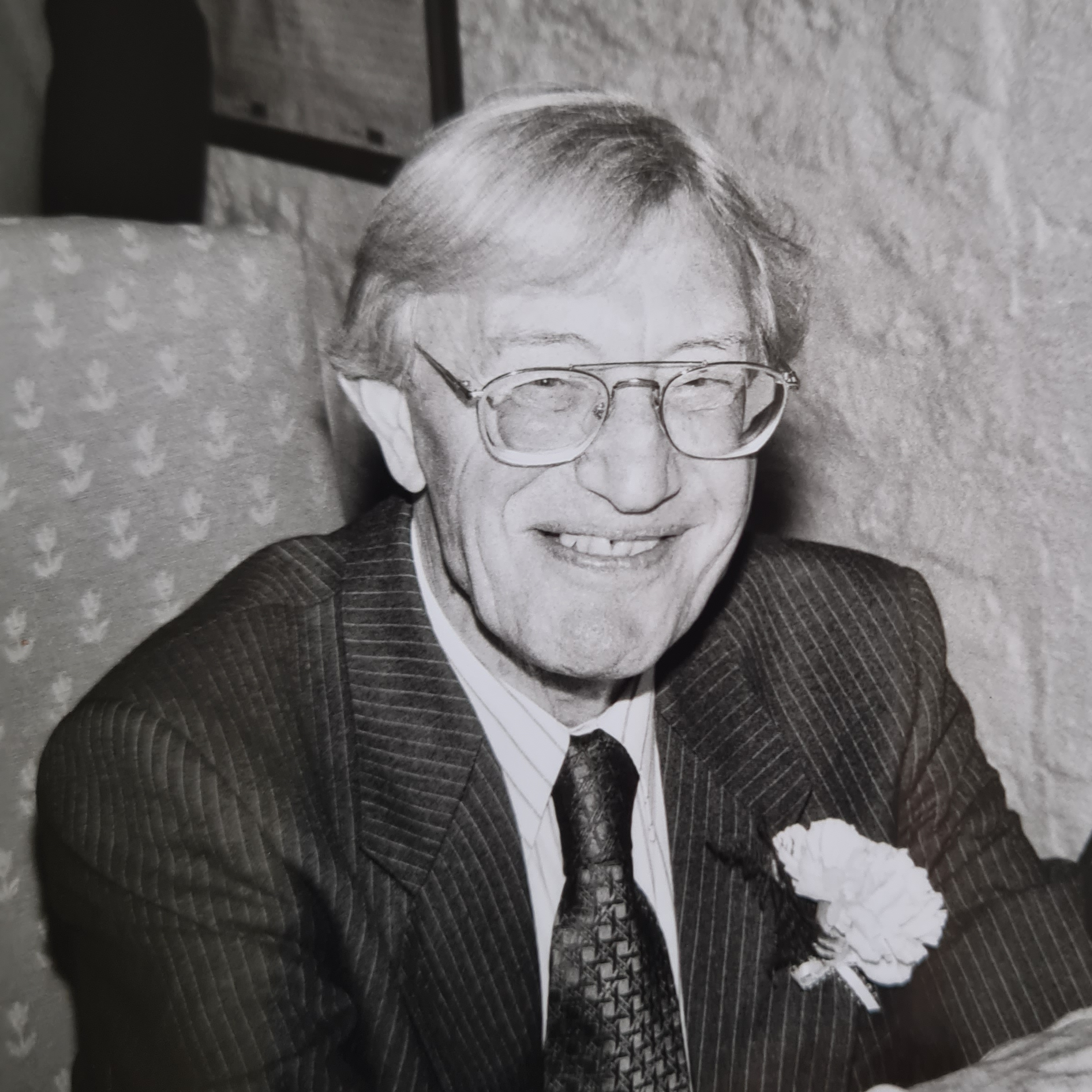 A black and white image of a smiling man wearing a suit and glasses with his hair swept to one side.