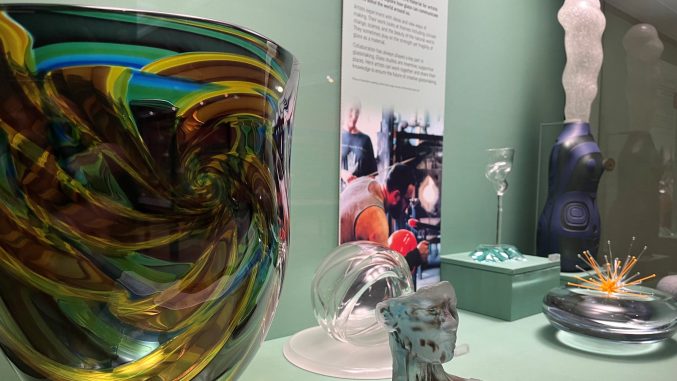colourful glass objects sit in a display case in a green gallery