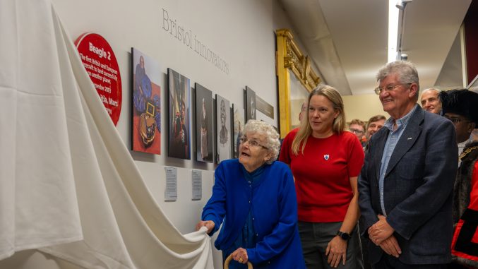 a woman pulls down a white curtain to unveil a plaque